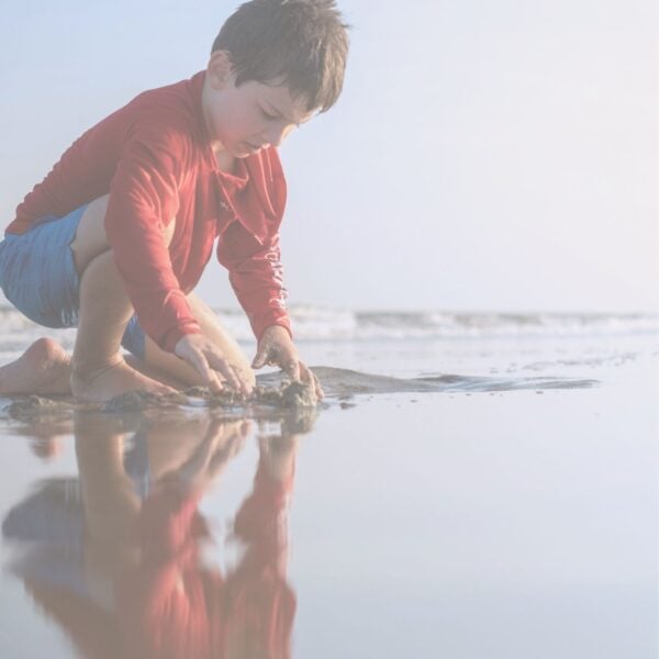 Reflector body playing in the shallow water at a beach with his reflection showing.